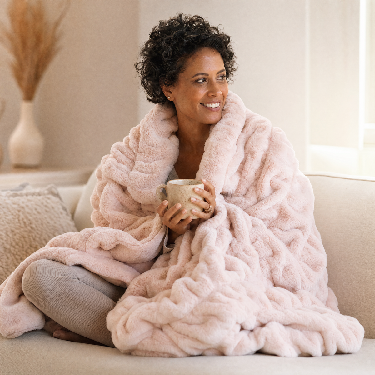 Woman wrapped in the Embrace plush hug blanket on the sofa